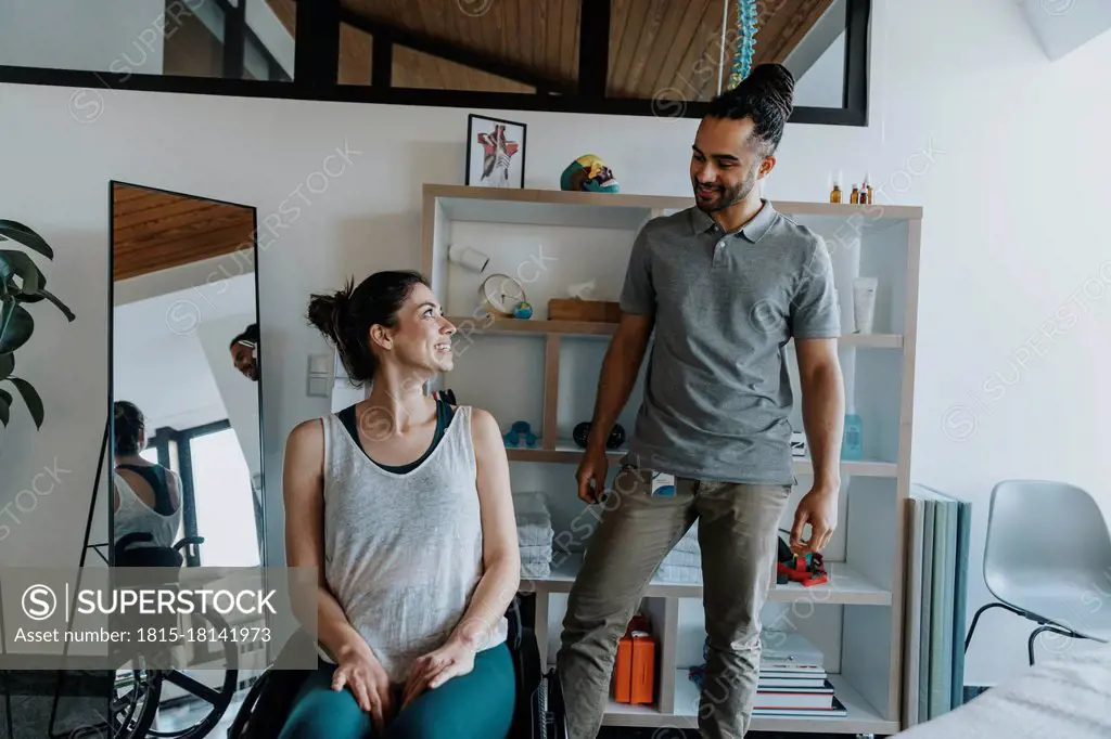 Smiling physiotherapist with female patient sitting on wheelchair in medical practice