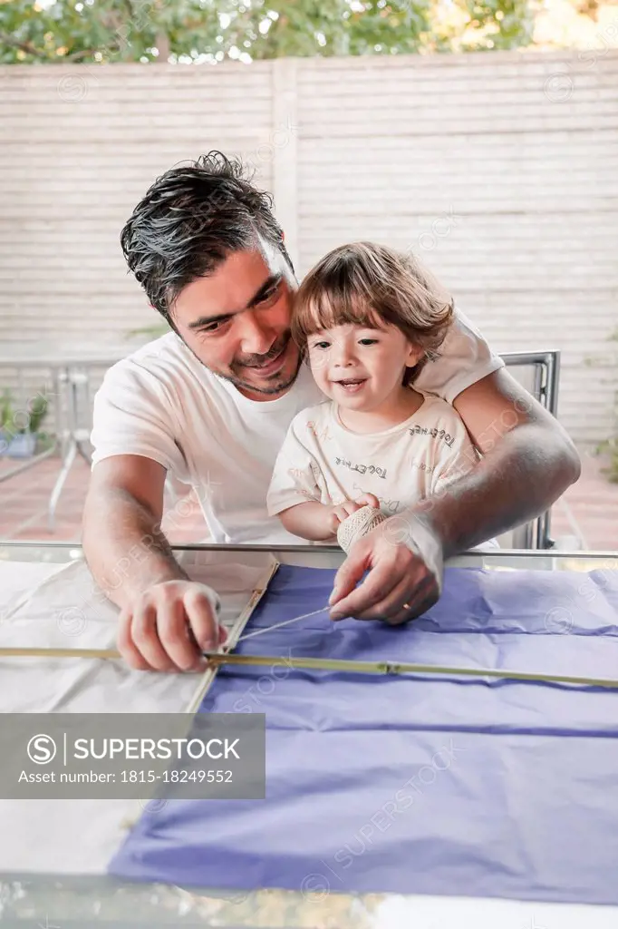 Father making kite with son in back yard