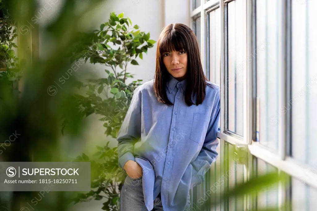 Beautiful woman with hands in pockets leaning on window at home