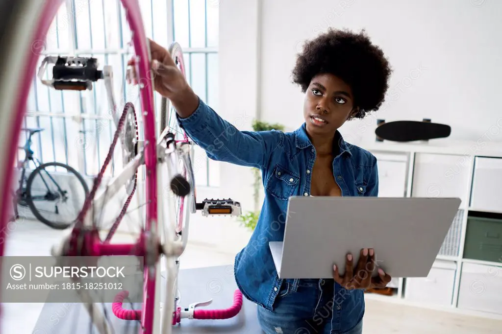 Woman using laptop while examining bicycle at home