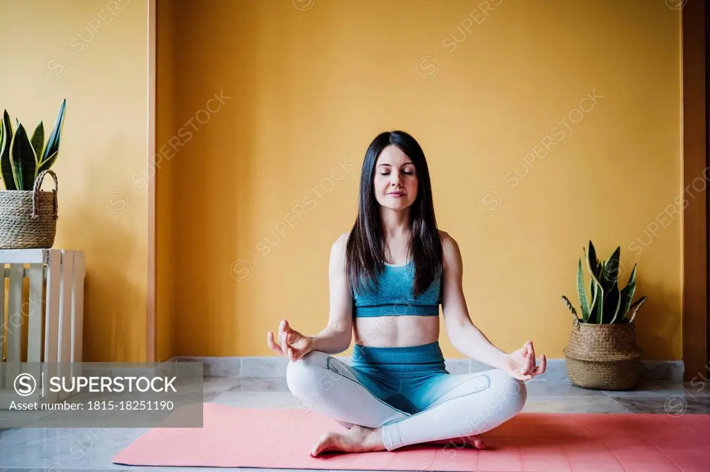 Sportswoman meditating while sitting on exercise mat at home