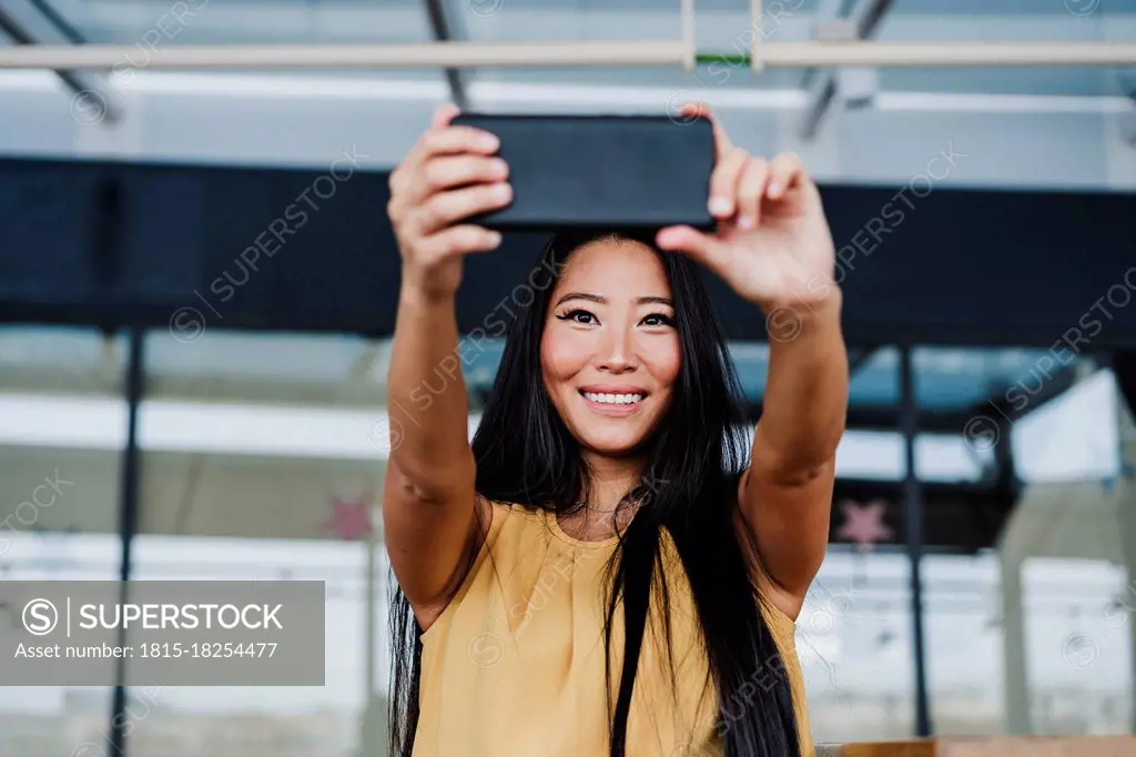 Happy businesswoman taking selfie from smart phone at office cafeteria