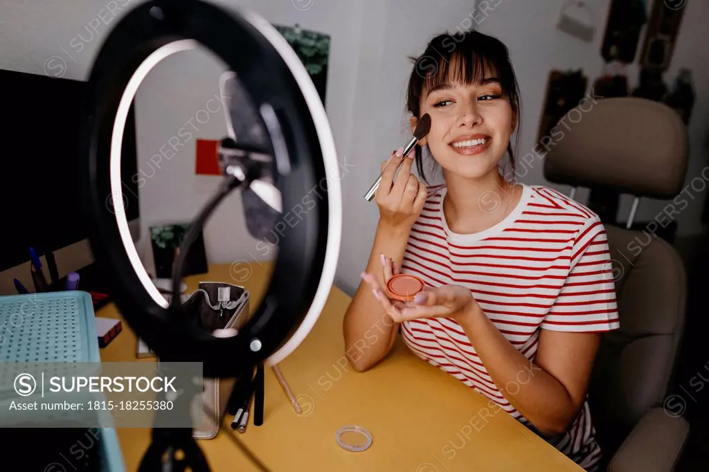 Female influencer vlogging while applying make-up at studio