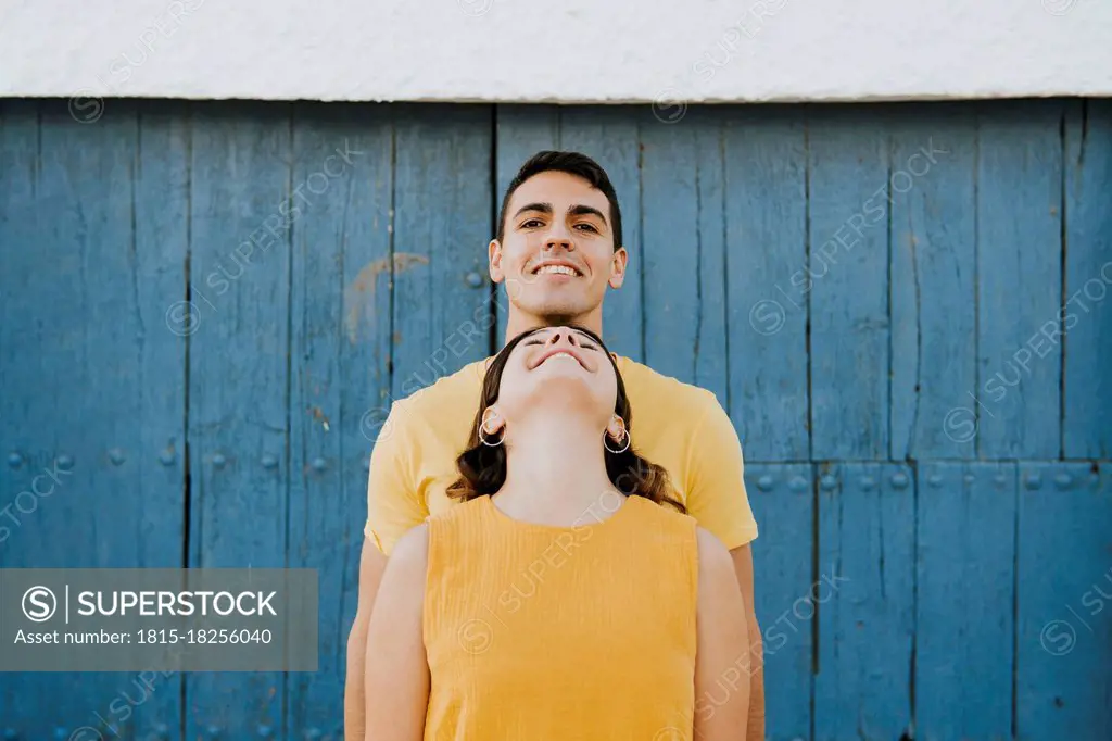 Young woman leaning on smiling man in front of wall