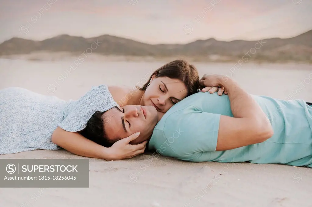 Young woman leaning on man at beach during sunset