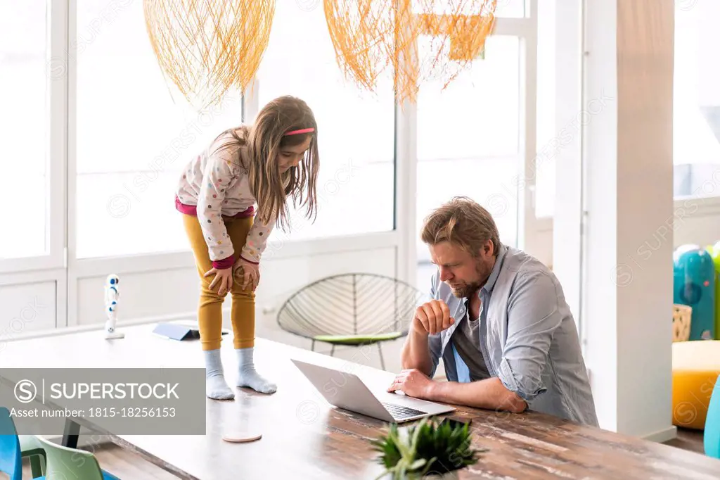 Businessman using laptop by daughter standing on table at home