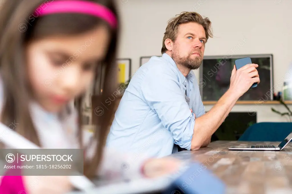 Thoughtful businessman looking away by daughter at home