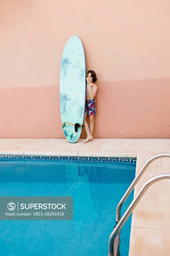 Pre-adolescent boy standing with surfboard at poolside