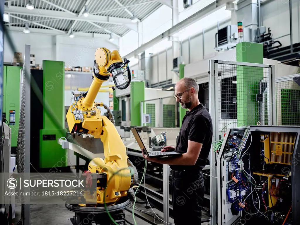 Male engineer using laptop by robotic arm