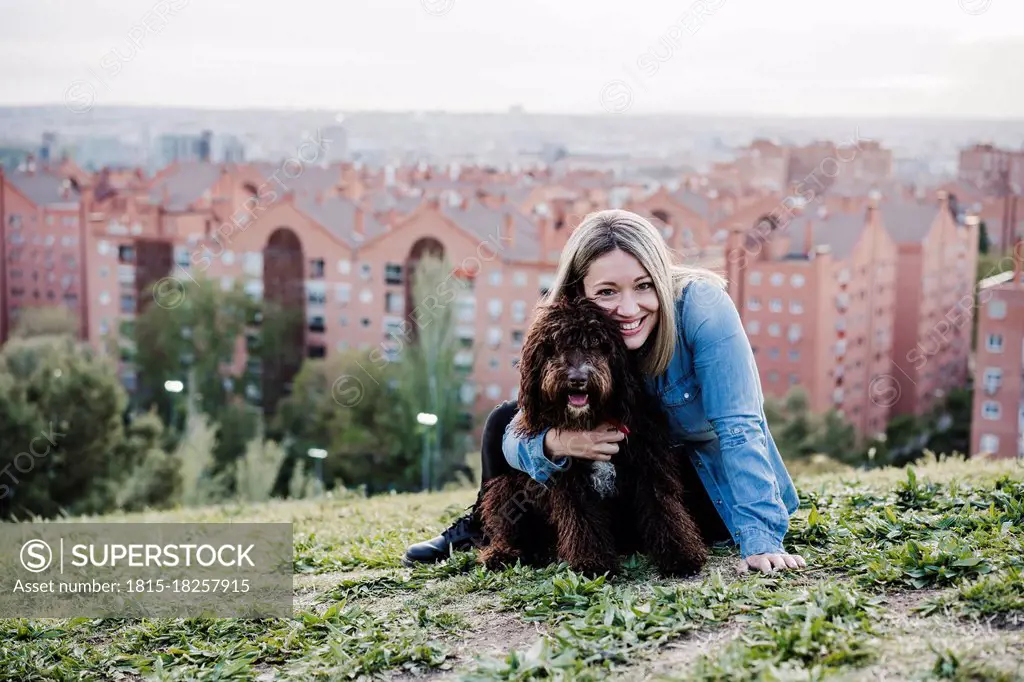 Happy woman embracing Spanish Water Dog in front of cityscape