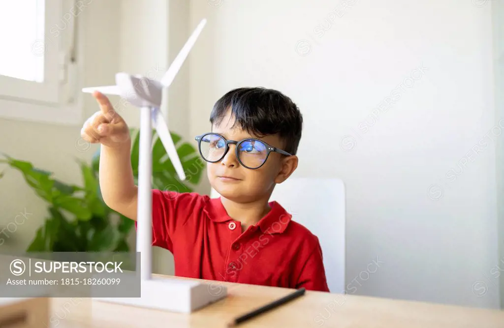 Boy wearing eyeglasses playing with wind turbine model at home