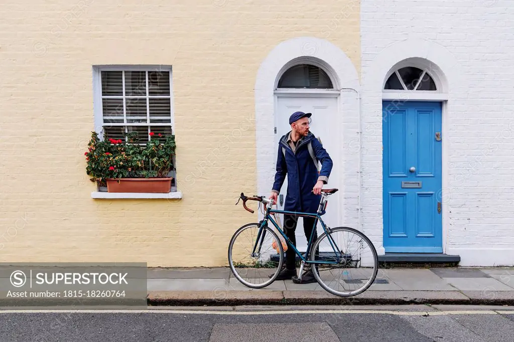 Young man looking away while holding bicycle on footpath