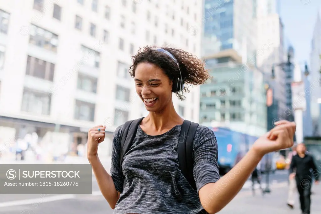 Cheerful woman dancing while listening music through headphones in city