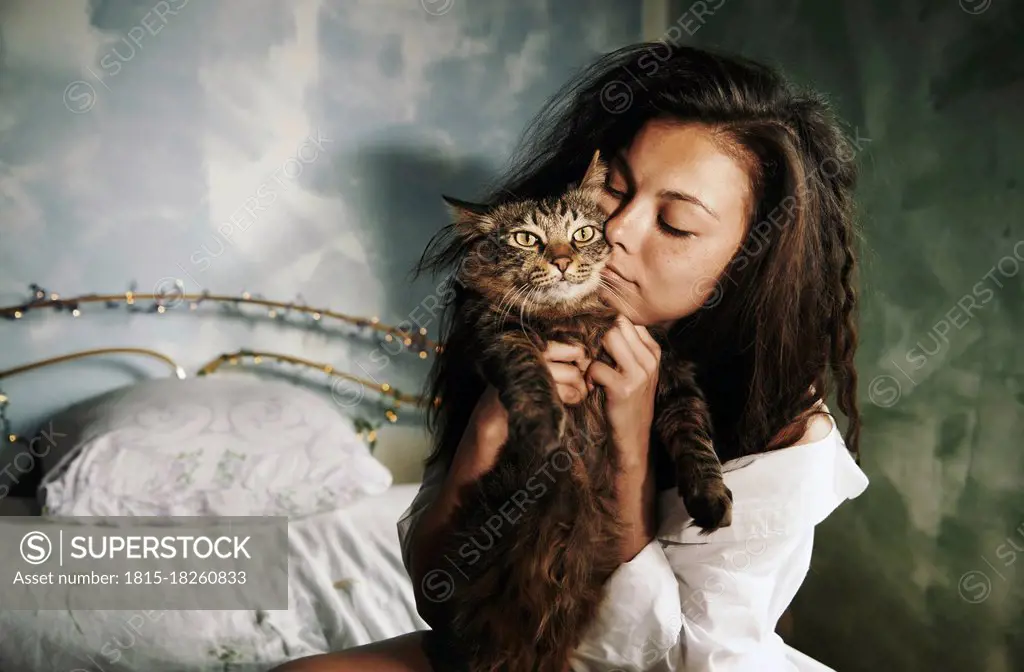 Woman embracing cat while sitting in bedroom