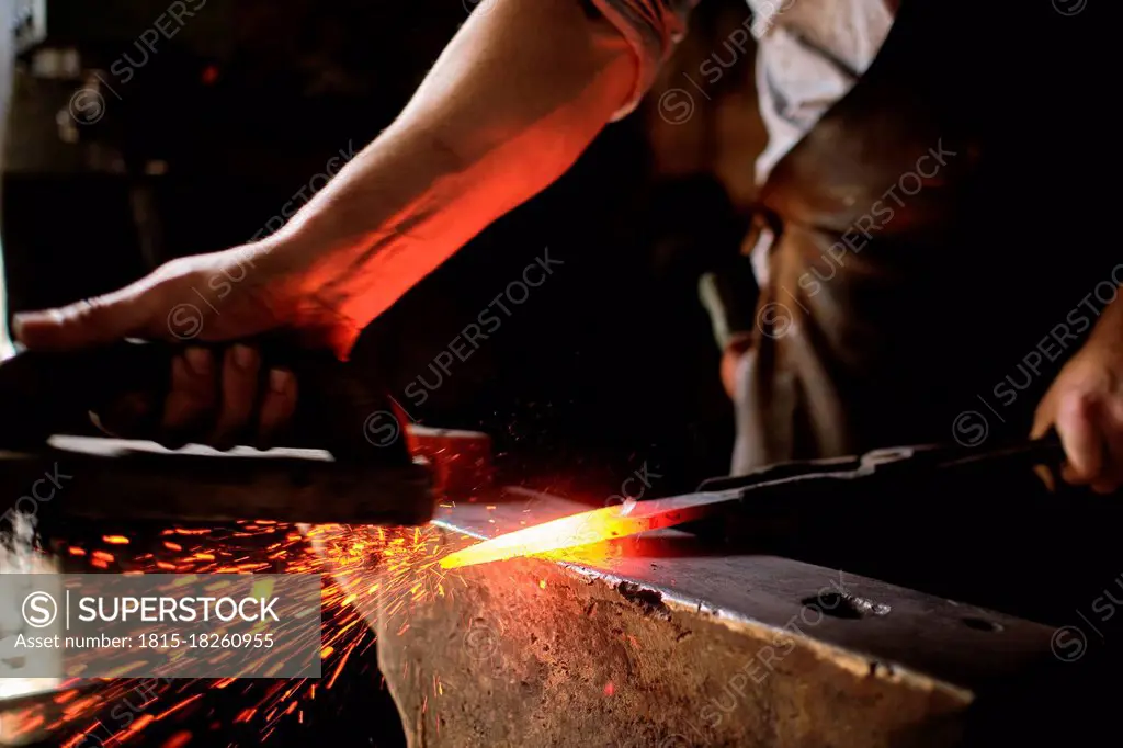 Male expert forging overheated metal on anvil at blacksmith shop