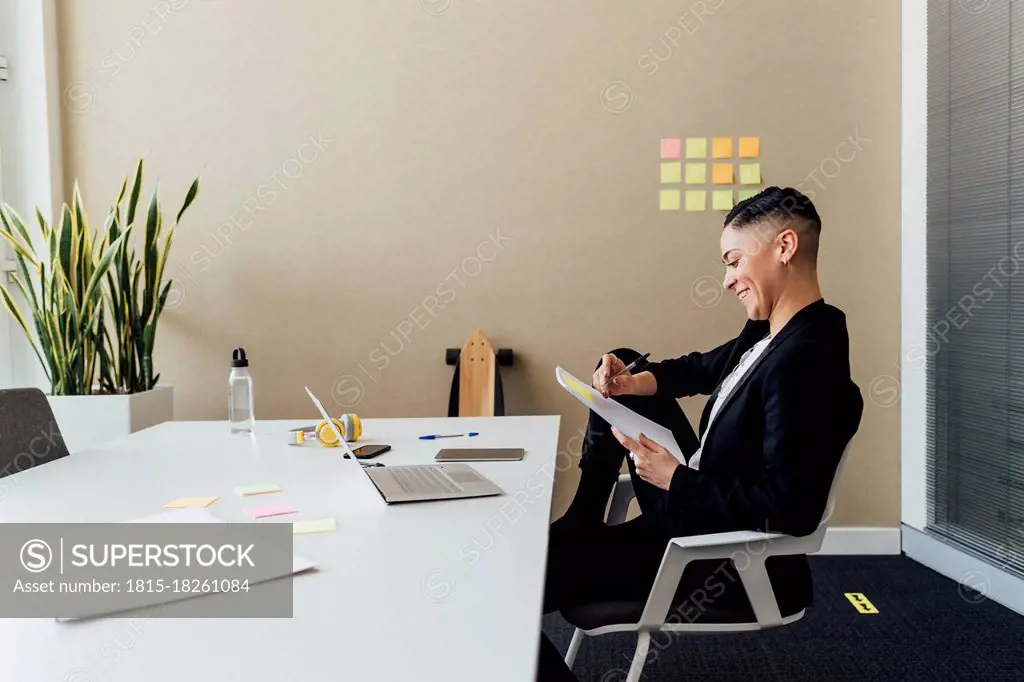 Smiling businesswoman writing on paper while sitting at desk in office