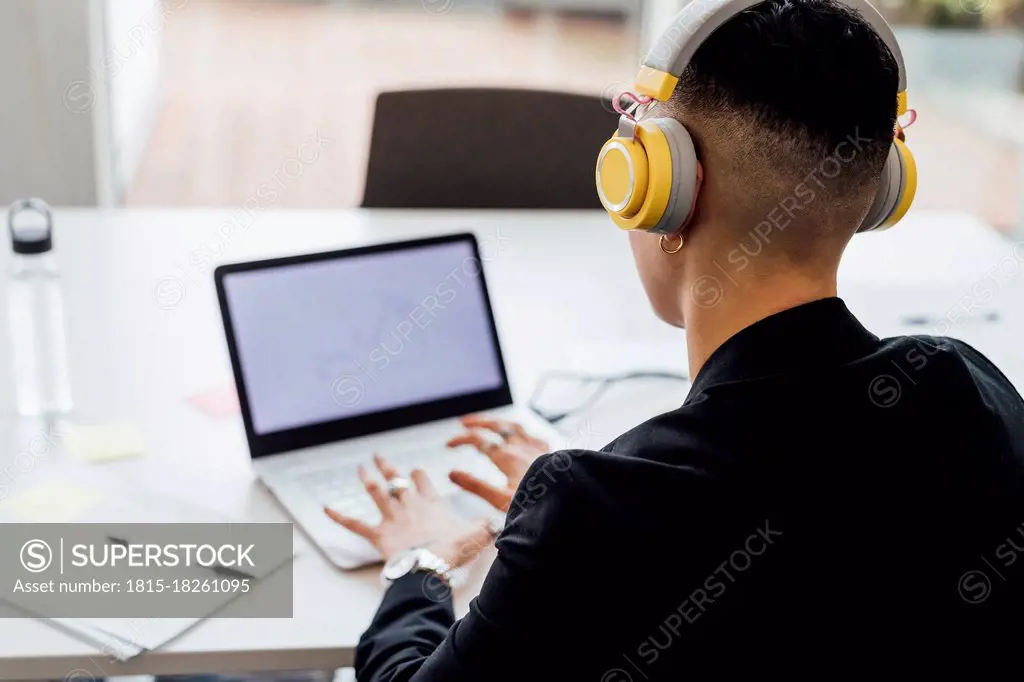 Female entrepreneur with headphones working on laptop in office