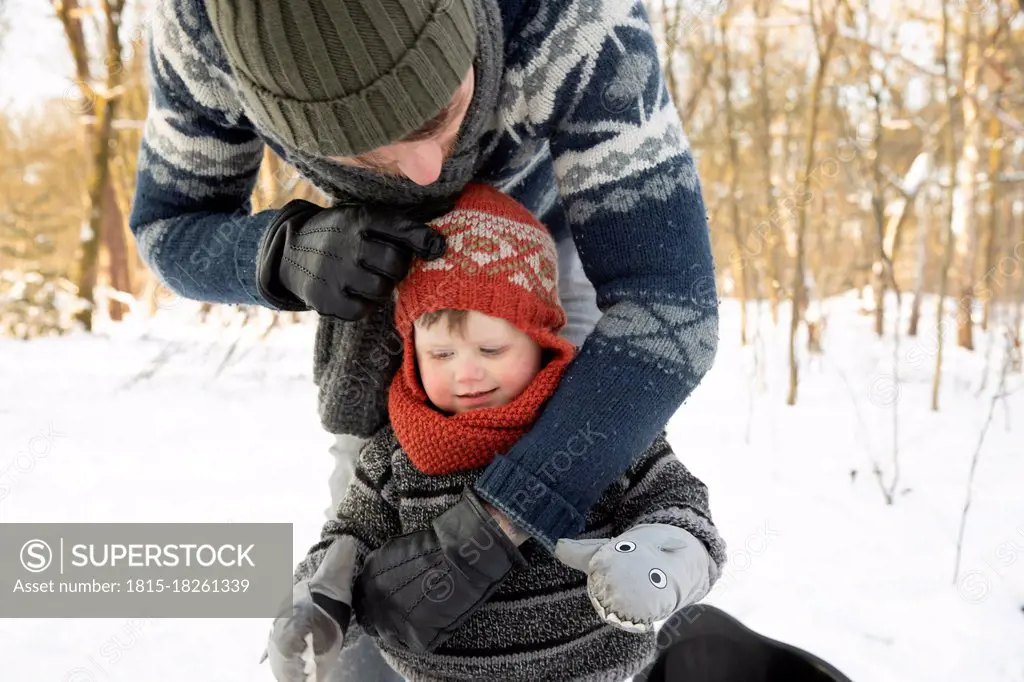 Father adjusting knit hat of son during winter