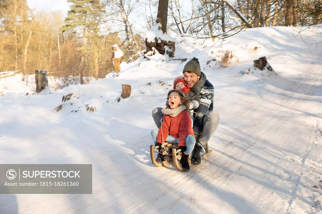 Playful boy sledding with father and brother on snow during winter