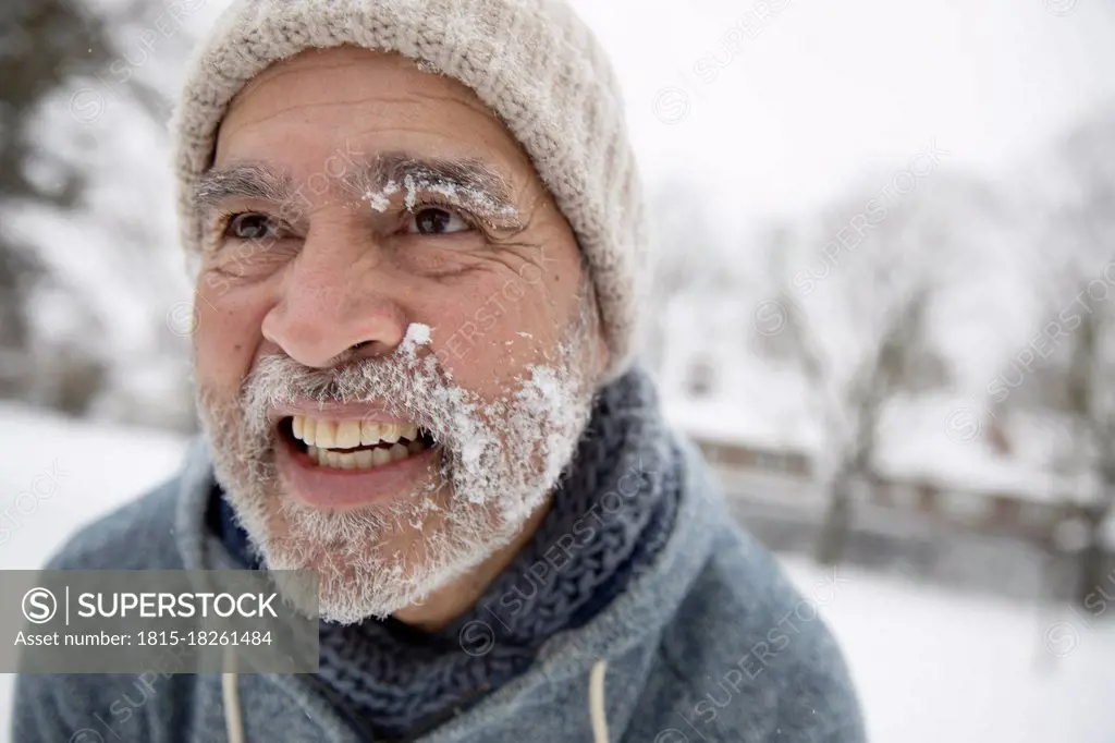 Smiling man looking away with snow on face during winter