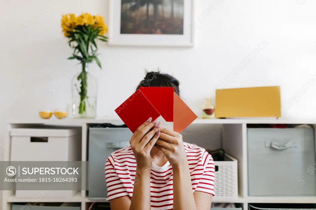 Young woman holding red color swatch in front of face at home