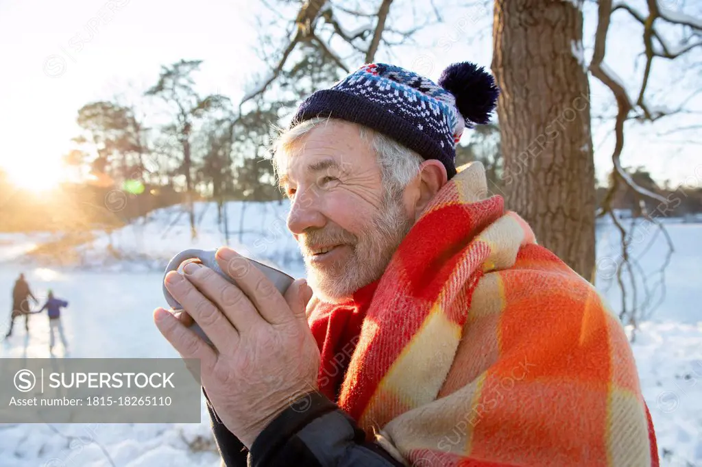 Senior man wrapped in blanket looking away while holding cup during winter