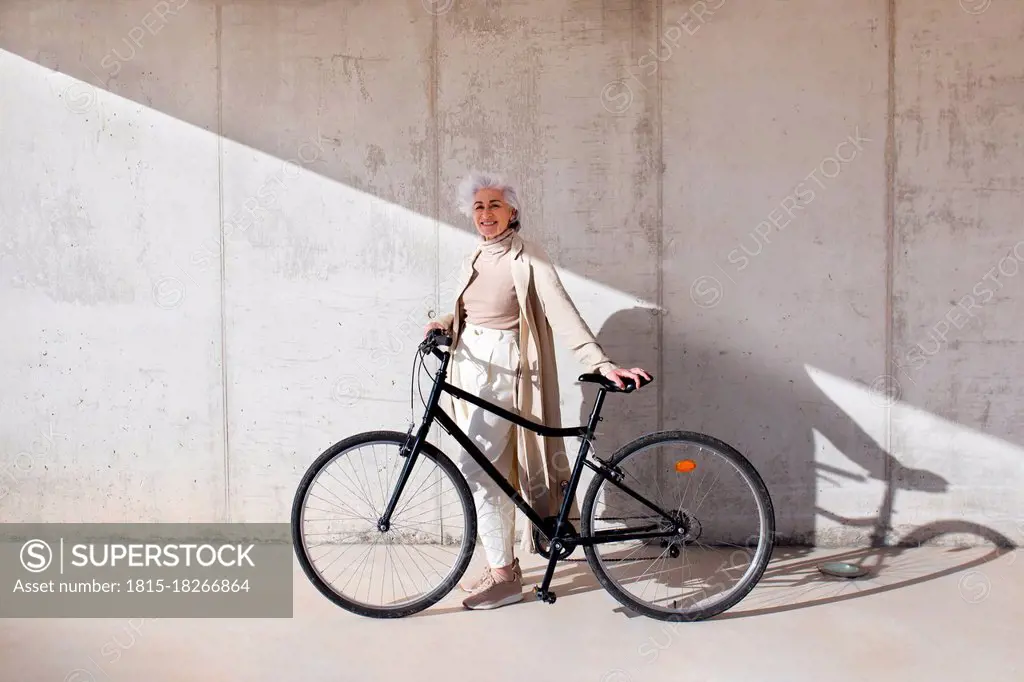 Smiling woman standing with bicycle on footpath