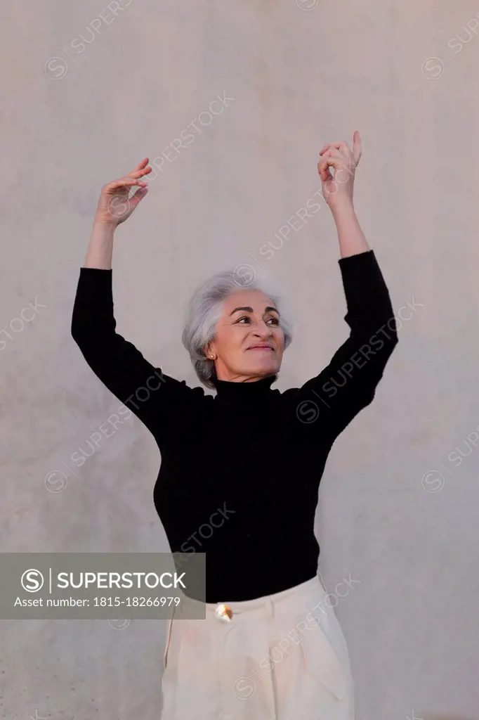 Mature woman looking away while dancing in front of wall