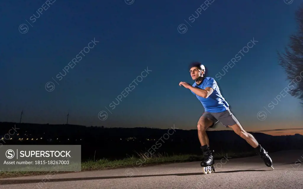 Young man with speed skating on road during dusk