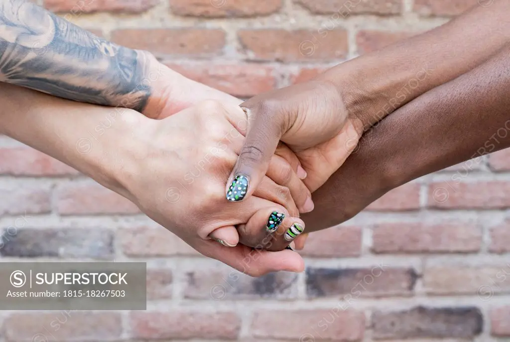 Multi-ethnic female friend holding hands in front of brick wall