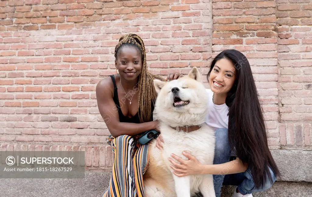 Multi-ethnic female friends with Akita Dog by brick wall