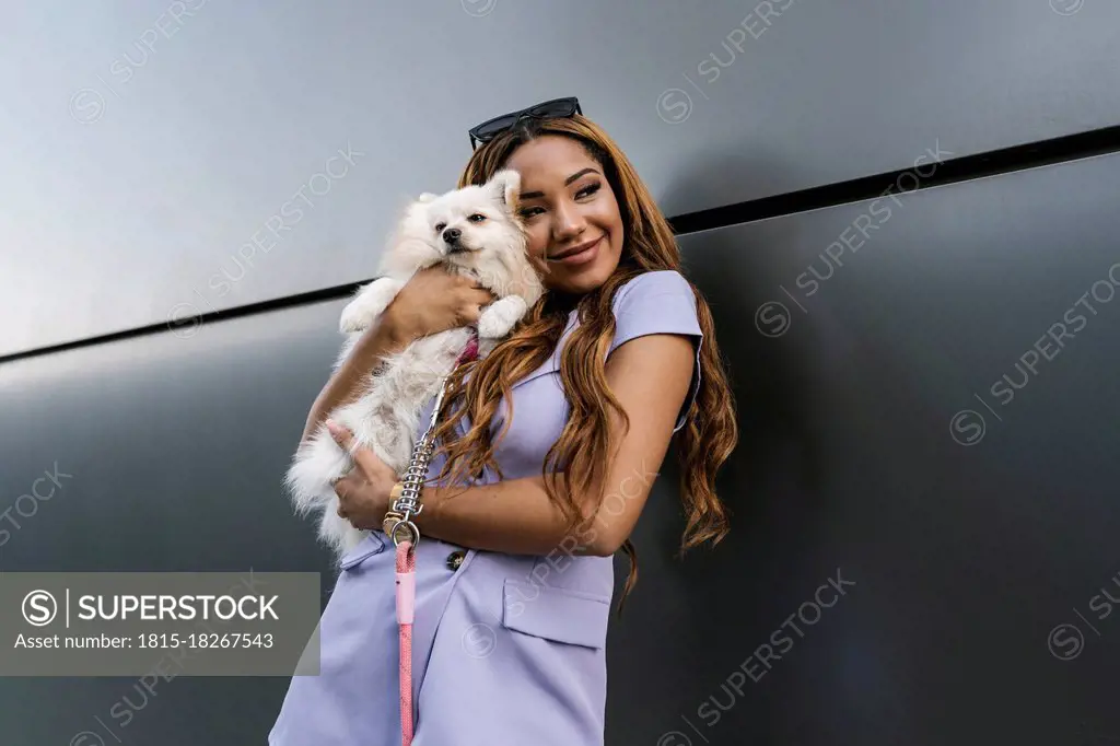 Young woman embracing dog while standing in front of gray wall