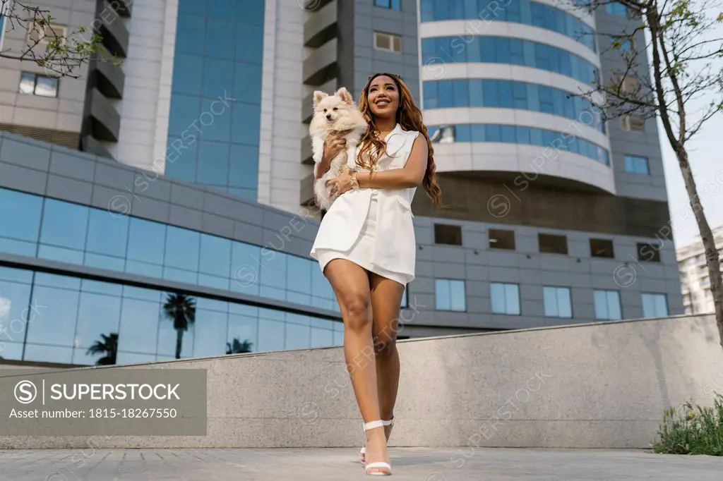 Stylish woman holding dog while walking on footpath