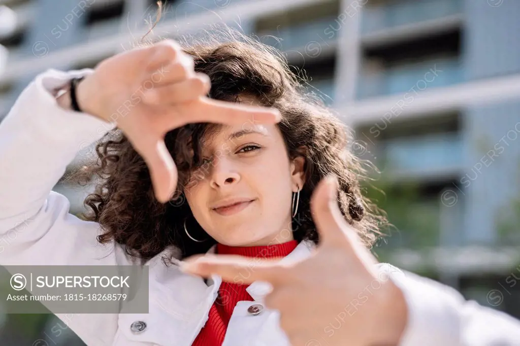 Young woman making finger frame with hands on sunny day