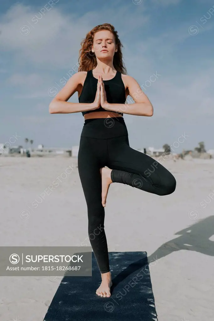 Young woman practicing tree pose at beach during sunny day