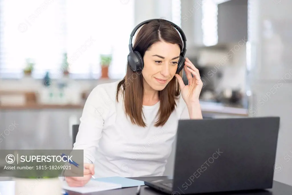 Smiling female entrepreneur wearing headphones working at home