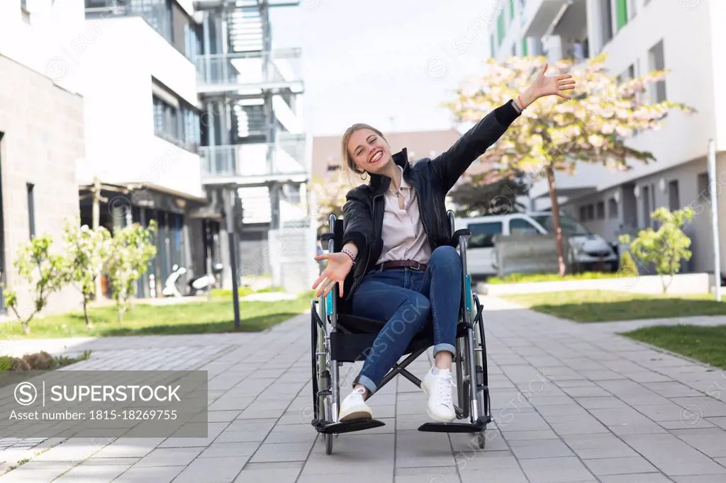 Happy disabled woman with arms outstretched sitting on wheelchair in residential area