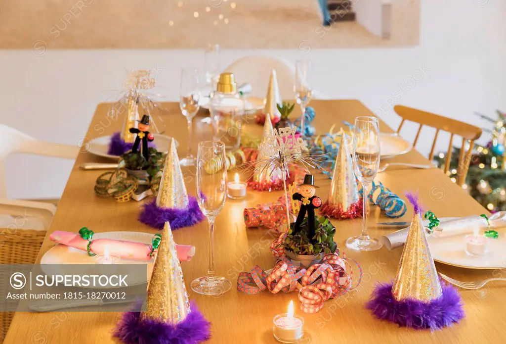 Festive laid New Years Eve table with plates, candles, party hats, champagne flutes and chimney sweep figurines