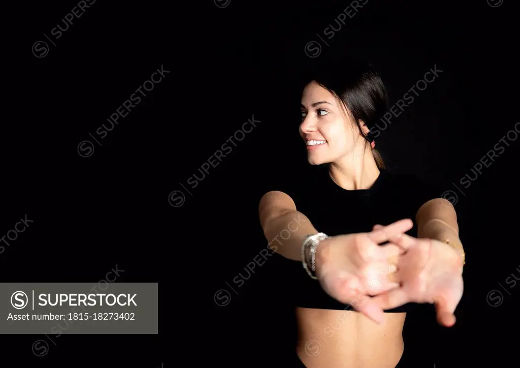 Smiling female athlete looking away while stretching in front of black background