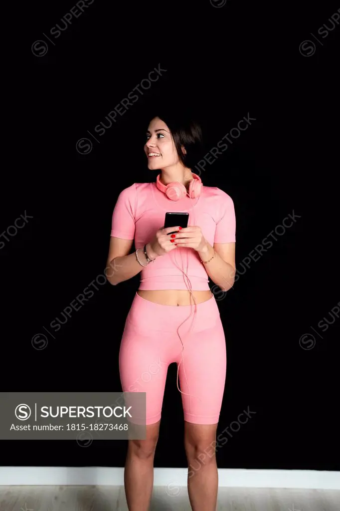 Smiling female athlete with mobile phone and headphones standing in studio