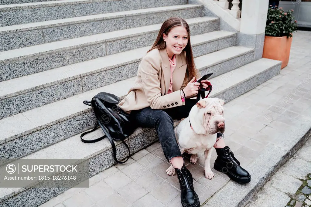 Smiling woman sitting with dog and mobile phone on steps