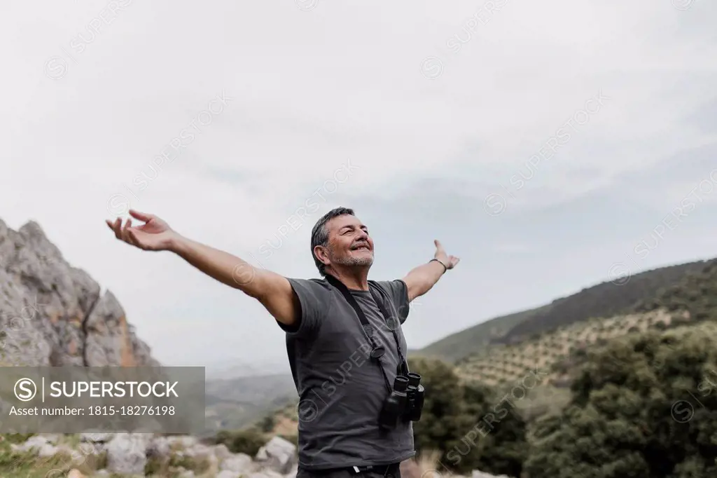 Carefree man standing with arms outstretched on mountain