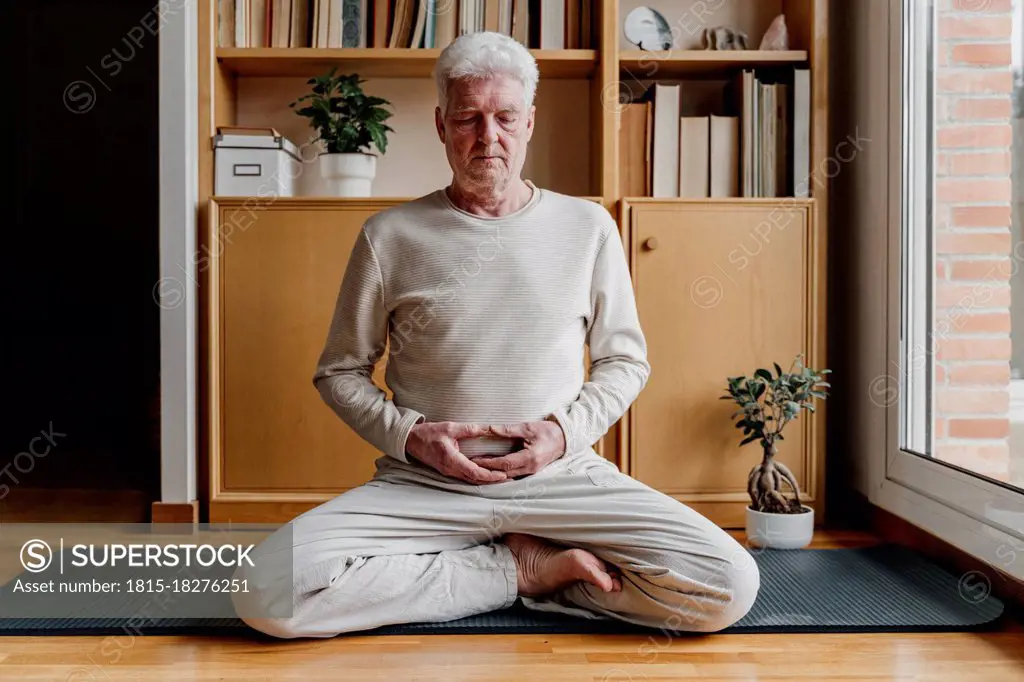 Senior man meditating while sitting with cross-legged at home