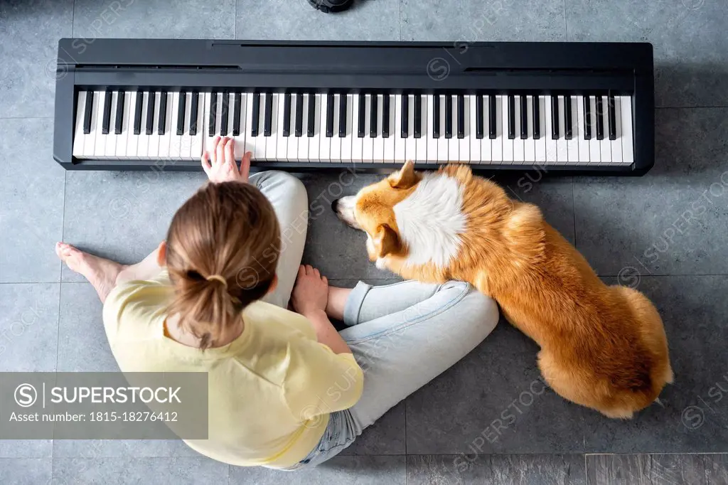 Mid adult woman sitting on floor while practicing playing piano at home