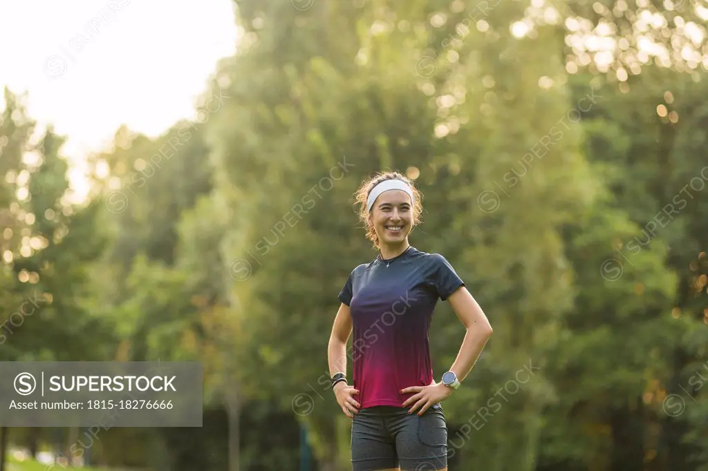 Smiling woman with hands on hip standing in public park