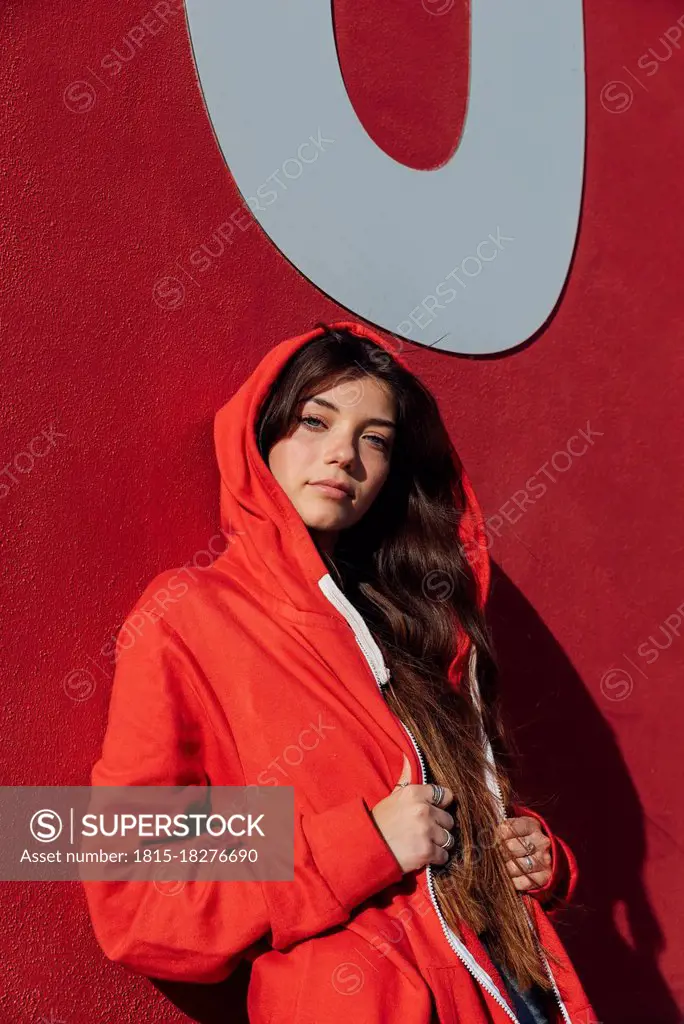 Teenage girl wearing red jacket while leaning on wall