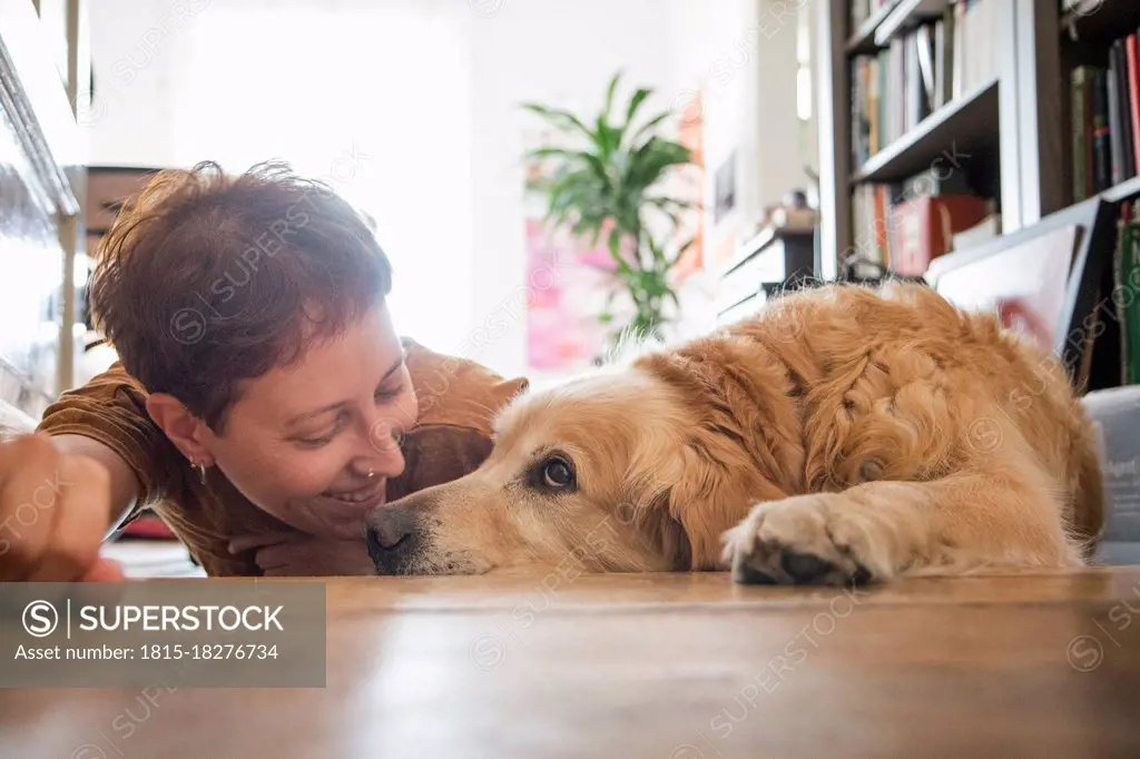 Smiling woman looking while lying with tired dog on parquet floor at home