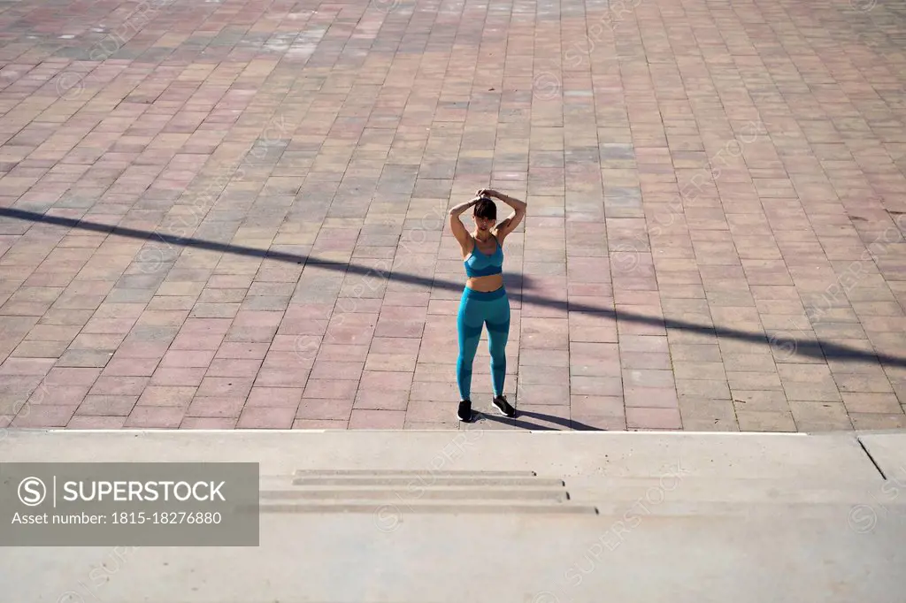 Female athlete tying hair in front of steps during sunny day