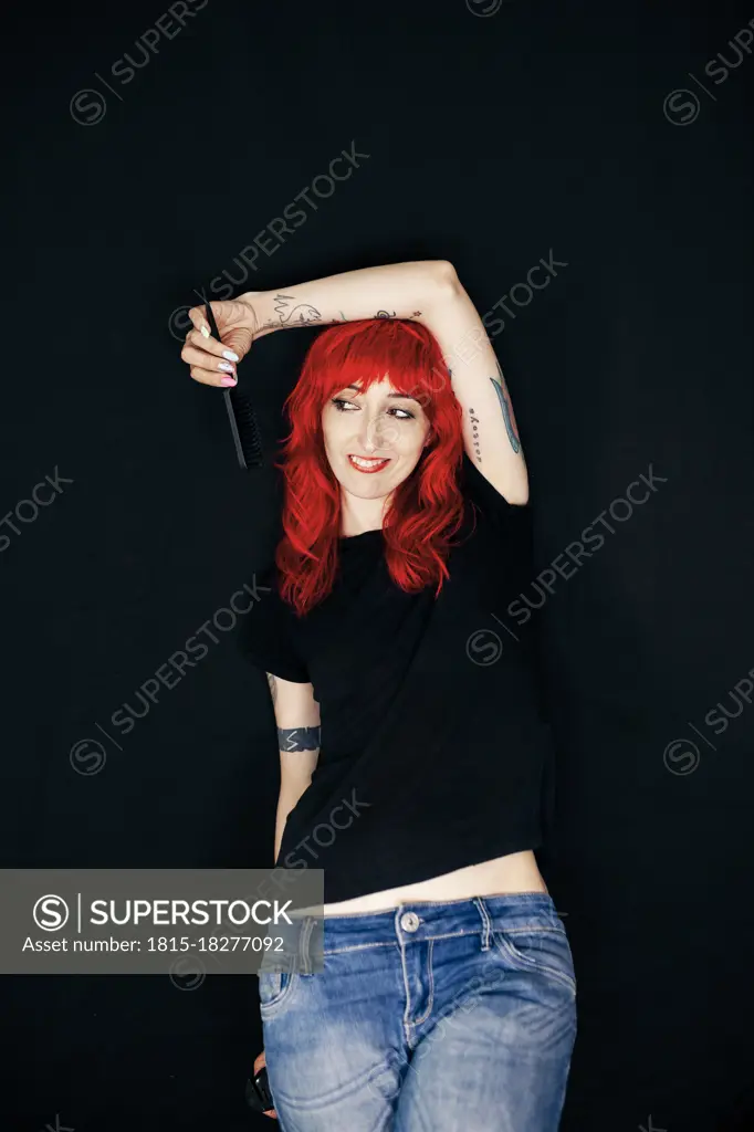 Beautiful female hairstylist with hand raised holding comb over black background