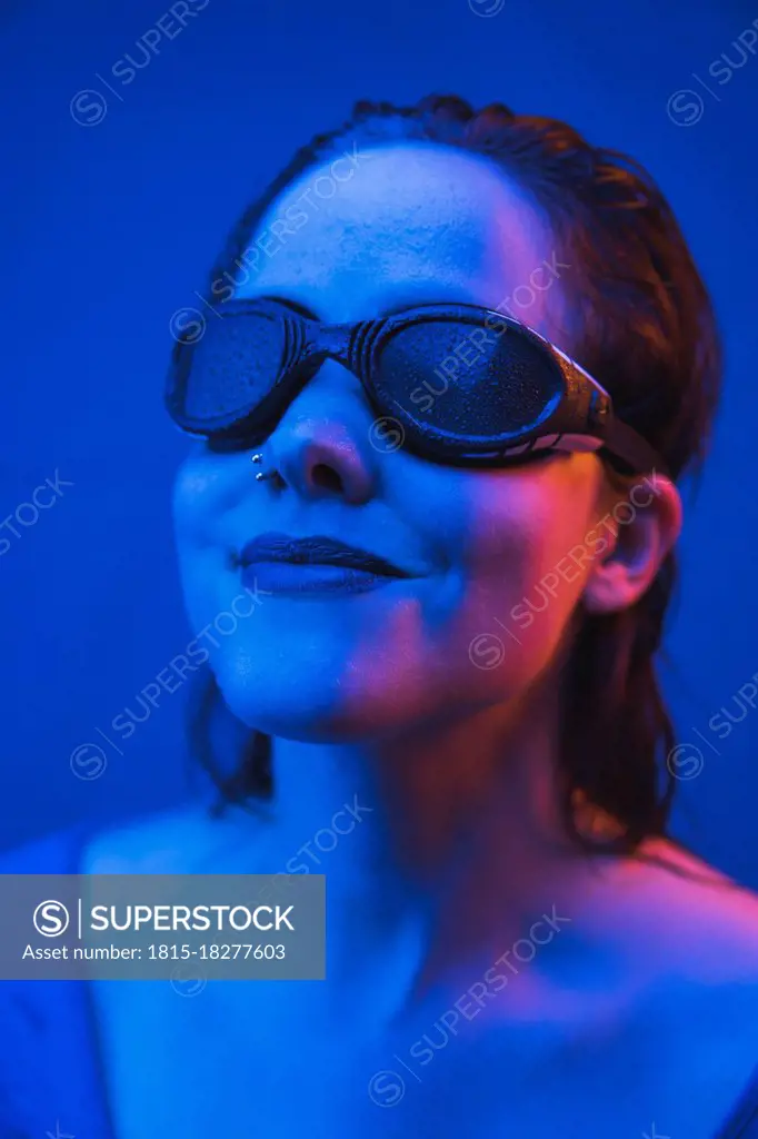 Beautiful woman wearing swimming goggles in front of blue background